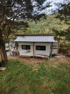 a small white trailer parked next to a tree in the woods with a metal roof