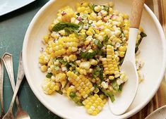 a white bowl filled with corn on top of a table next to utensils