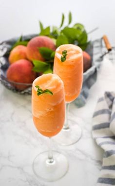 two wine glasses with peaches in them on a marble table next to some fruit