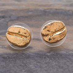 two gold earrings sitting on top of a stone floor next to each other and one has a piece of bread in it's middle