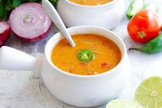 two white bowls filled with soup next to sliced onions and limes on a table