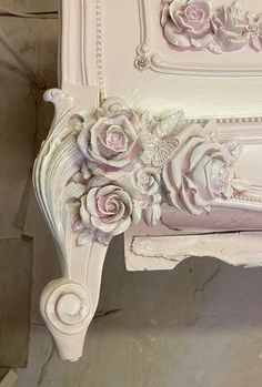 an ornate white bench with pink roses on the back and sides, sitting in a room