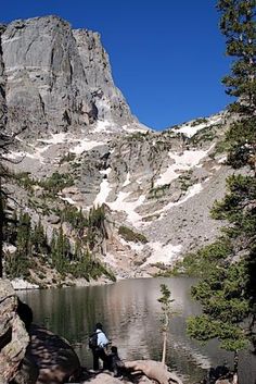 two people sitting on rocks near a mountain lake