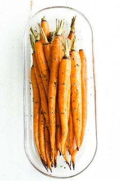 carrots with herbs in a glass dish on a white table top, ready to be cooked