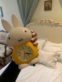 a person holding a clock shaped like a rabbit on top of a bed in a bedroom