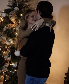 a man and woman embracing in front of a christmas tree