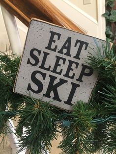 a sign that says eat sleep ski hanging from the side of a building with pine branches