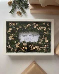 a christmas wreath with pine cones and greenery is displayed in a white frame next to presents