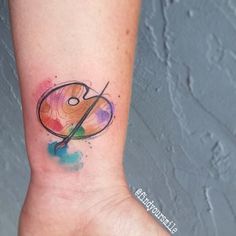 a small tattoo on the wrist of a woman with scissors and paint splatters