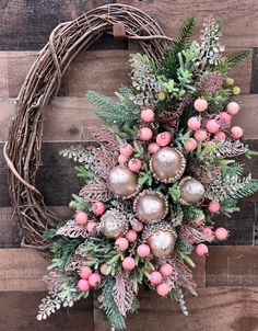 a wreath with pink and green decorations hanging on a wooden wall