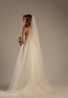 a woman in a wedding dress with a veil on her head and flowers in her hand