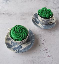 two teacups with green frosting on them sitting next to eachother