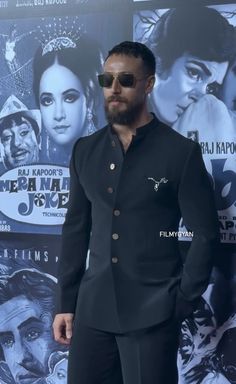 a man in a black suit and sunglasses standing on a red carpet next to a movie poster