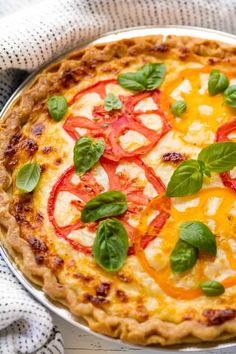 a pizza with cheese, tomatoes and basil on it sitting on top of a table