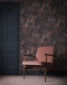 a pink chair sitting in front of a wallpapered room with an open door