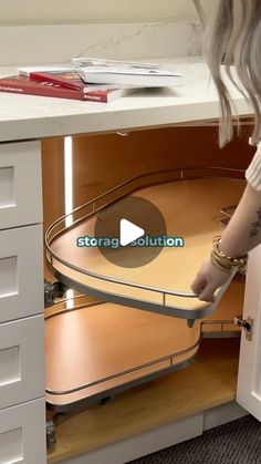 a woman is opening the bottom drawer of a kitchen cabinet with an adjustable pull out tray