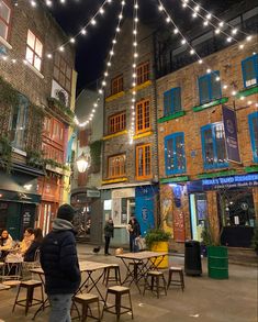 people are sitting at tables in the middle of an alleyway with lights strung overhead