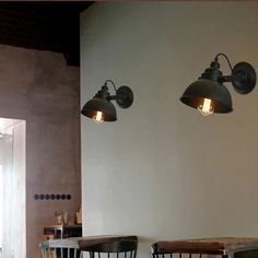 two lamps are hanging on the wall above tables