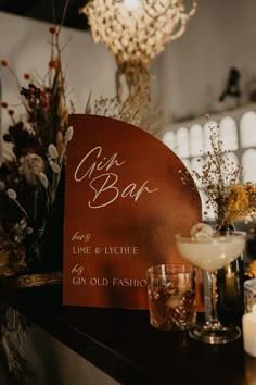 a bar sign sitting on top of a wooden table next to candles and glasses filled with drinks