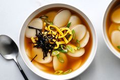 two bowls filled with soup on top of a white table next to silver spoons