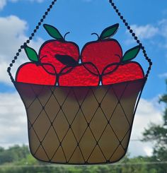 a stained glass window with apples in a basket hanging from it's side, against a blue sky background