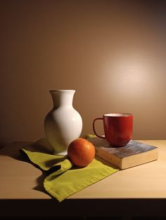 a white vase sitting on top of a table next to an orange and a book