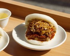 two white plates with food on them sitting on a wooden table next to a cup