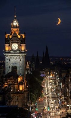 a clock tower in the middle of a city at night with traffic passing below it