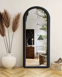 a mirror sitting on top of a wooden floor next to a vase