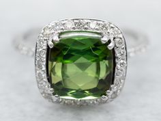 "This lovely green tourmaline halo ring is full of refined glamour! The white gold mounting is encrusted with glittering diamonds, allowing the ring to sparkle even in profile. The tourmaline is a rich, juniper green color that contrasts beautifully with the polish of the metal. Metal: 14K White Gold Gem: Green Tourmaline 2.53 Carats Gem Measurements: 8.0 mm, Square Cushion Cut Accents: 43 Diamonds totaling .50 Carats, G-H in Color, SI in Clarity Ring Size: 5.50 Marks: \"BB 14K\" Stamped on the inside band To view a video of this piece check out the link below: https://vimeo.com/825132359 SKU #: A26002 Each piece has been identified and graded by a Graduate Gemologist who has been certified by the Gemological Institute of America (GIA). We have six brick-and-mortar storefronts in Maine, Ma Ring Green Stone, Juniper Green, Green Stone Ring, Green Tourmaline Ring, Green Stone Rings, Pink Tourmaline Ring, Diamond Halo Ring, Ring White Gold, Blue Tourmaline