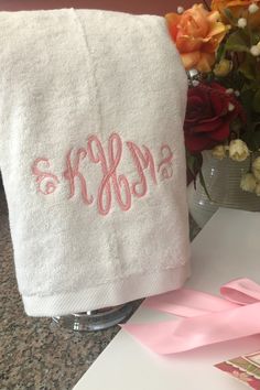 a white towel with the word monogrammed on it next to flowers and a pink ribbon