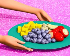 a child's hand reaching for some fruit on a green plate with blueberries, apples and cheese