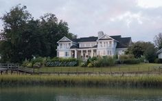 a large white house sitting on top of a lush green field next to a lake