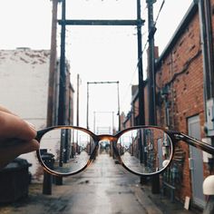 a hand holding up a pair of glasses in front of a brick building on the street