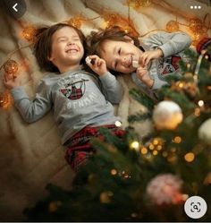 two young children laying next to each other in front of a christmas tree with lights