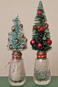 two small christmas trees in glass vases on a table