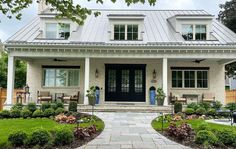 a white brick house with black doors and windows on the front porch is surrounded by greenery