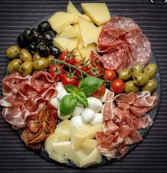 an assortment of cheeses, meats and olives arranged in a circle on a plate