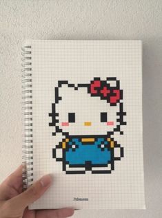 a hand holding a notebook with an image of a hello kitty in blue overalls