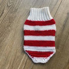 a red and white crocheted dog sweater on a wooden floor with wood floors