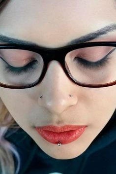 a woman with eye glasses and piercings on her nose is looking at the camera