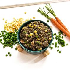 a bowl filled with meat, peas and carrots next to some other vegetables on a white surface