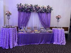 the table is covered with purple linens and flowers, along with cupcakes