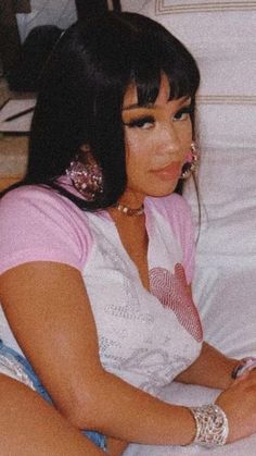 a woman sitting on top of a bed next to a white blanket and pillows with her hand resting on the pillow