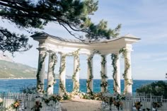 an outdoor wedding set up by the ocean with flowers and greenery on the pillars