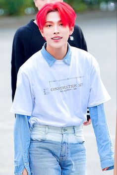 a young man with red hair wearing a white shirt and blue jeans, walking down the street