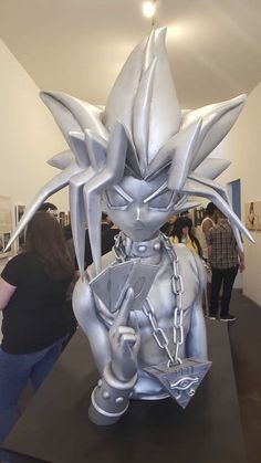 a silver statue is on display at an art gallery with people in the background looking at it