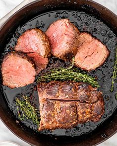 steaks and potatoes cooking in a skillet on a marble counter top, with rosemary sprigs