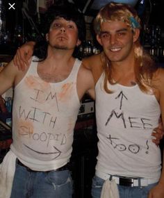 two young men standing next to each other wearing tank tops with writing on their vests