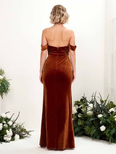 the back of a woman in a brown velvet dress standing next to flowers and greenery